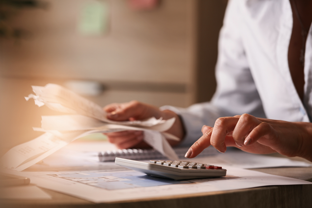 Close up of businesswoman using calculator while going through financial bills. Close up of accountant holding bills and working on calculator in the office.