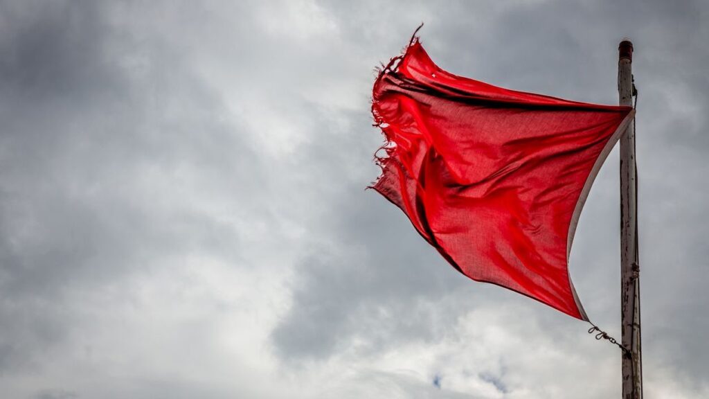 A wind torn red warning flag indicating danger on an English beach.